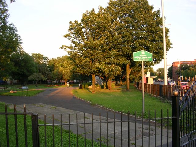 A black gated park entrance with a green welcome sign to Ardwick Green Park Manchester
